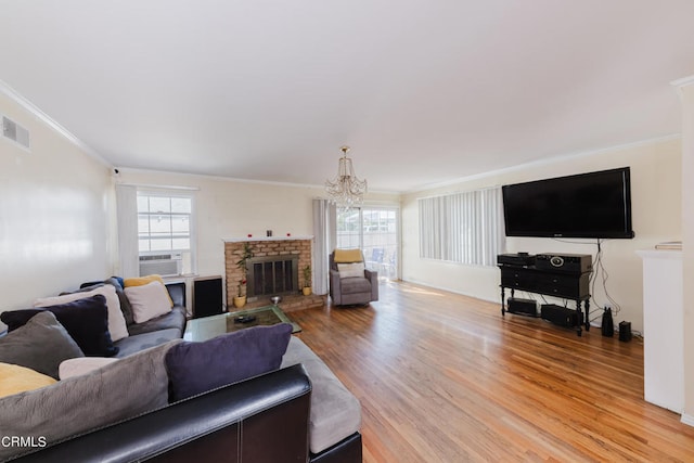 living room with wood-type flooring, a notable chandelier, a fireplace, and crown molding