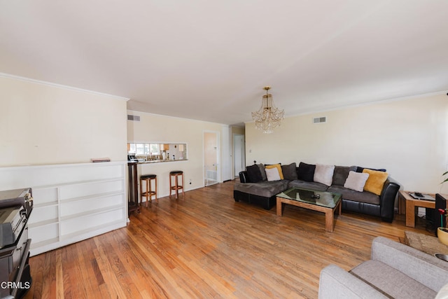 living room with ornamental molding, a chandelier, and light hardwood / wood-style floors