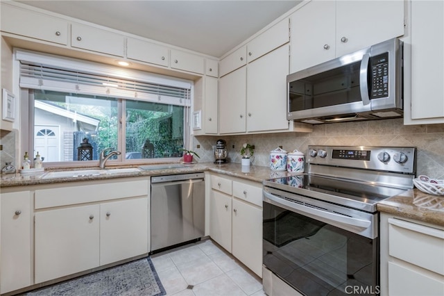 kitchen featuring white cabinets, sink, light tile patterned floors, stainless steel appliances, and decorative backsplash