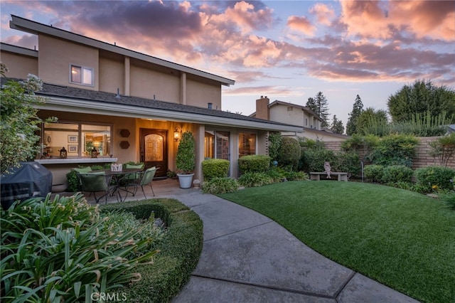 back house at dusk with a yard and a patio area