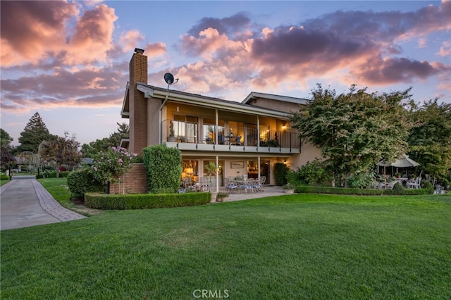 back house at dusk featuring a balcony and a yard