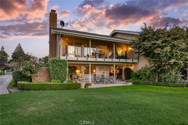 back house at dusk featuring a yard, a patio, and a balcony