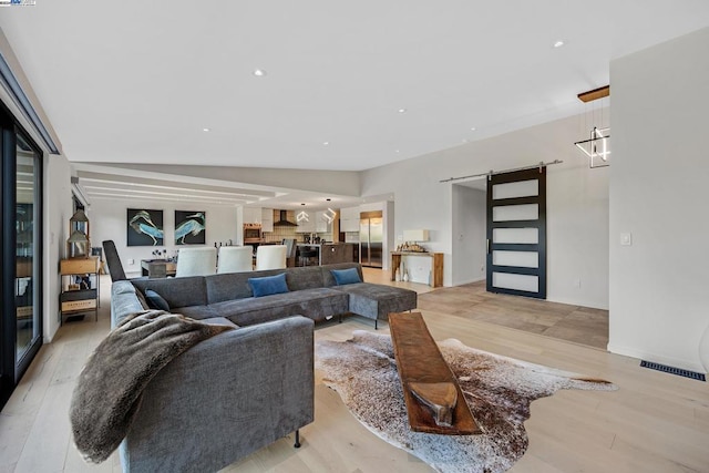 living room featuring a barn door, vaulted ceiling, and light hardwood / wood-style flooring