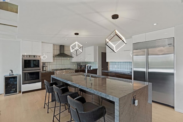 kitchen featuring stainless steel appliances, white cabinets, wall chimney exhaust hood, sink, and decorative light fixtures