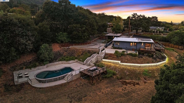 back house at dusk featuring a swimming pool with hot tub and a patio area