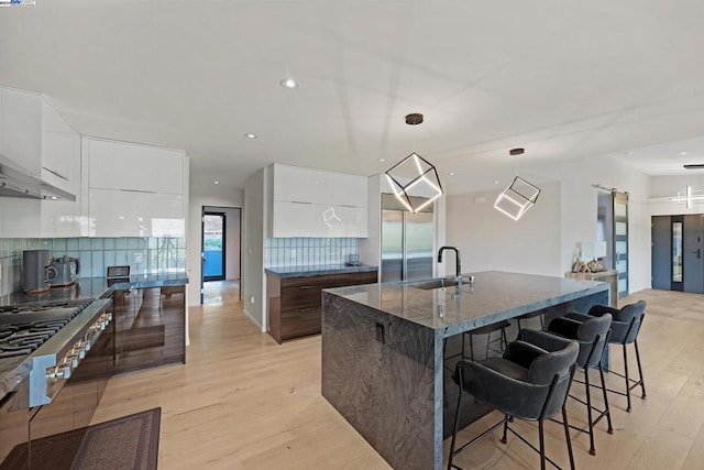 kitchen featuring light wood-type flooring, white cabinets, sink, a center island with sink, and backsplash