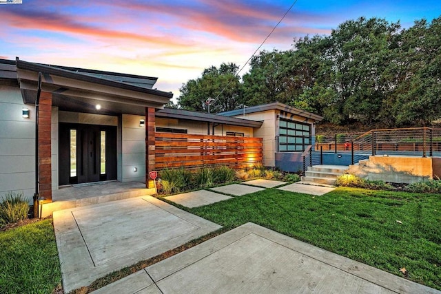 exterior entry at dusk featuring a lawn and a patio area