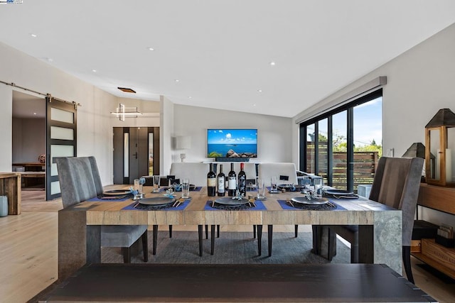 dining area with lofted ceiling, a barn door, and wood-type flooring