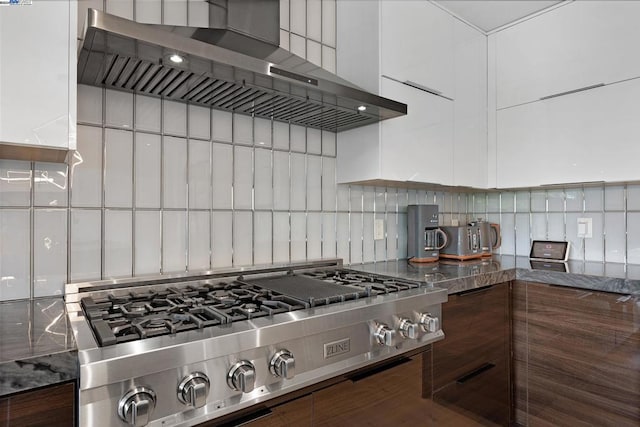 kitchen featuring wall chimney exhaust hood, dark stone countertops, stainless steel gas cooktop, and decorative backsplash