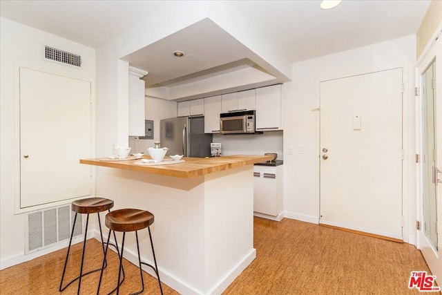 kitchen with wooden counters, appliances with stainless steel finishes, kitchen peninsula, white cabinets, and a breakfast bar area