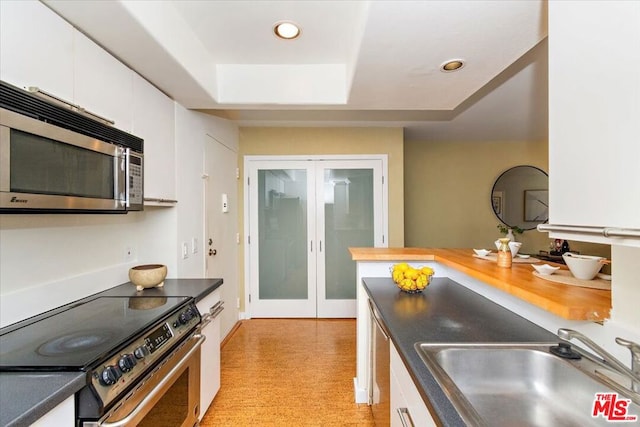 kitchen with white cabinets, sink, a tray ceiling, electric range oven, and light colored carpet