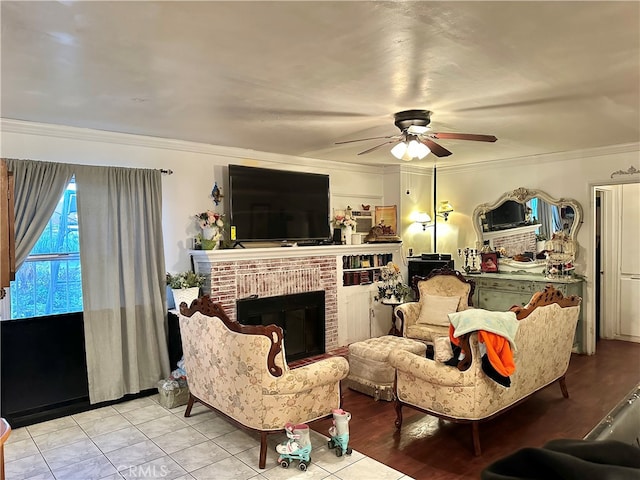 living room featuring crown molding, light tile patterned floors, a brick fireplace, and ceiling fan