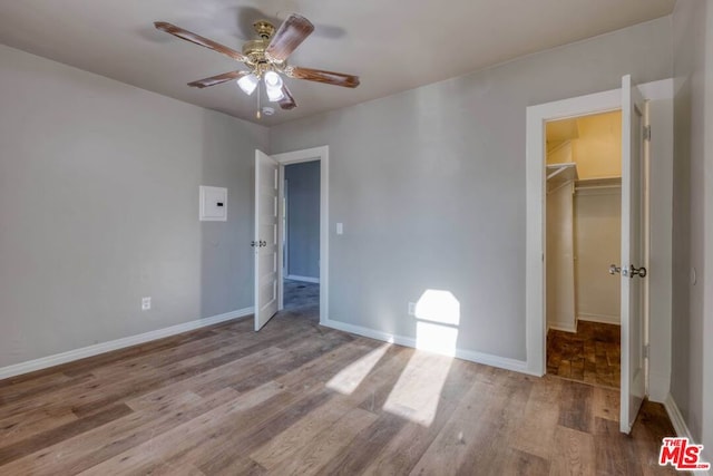 unfurnished bedroom featuring a closet, a walk in closet, light wood-type flooring, and ceiling fan