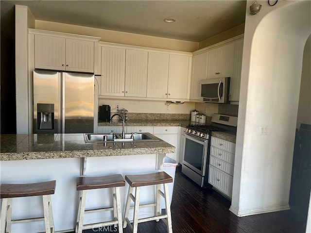 kitchen featuring a breakfast bar, sink, dark hardwood / wood-style floors, appliances with stainless steel finishes, and white cabinetry