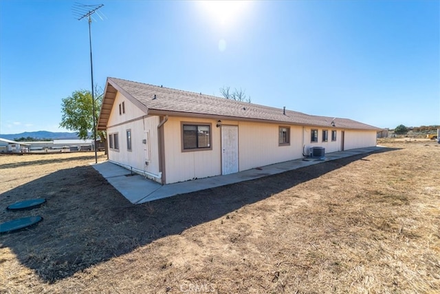 rear view of property with central AC unit, a mountain view, a lawn, and a patio area