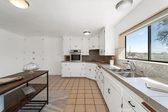 kitchen with white cabinets, tasteful backsplash, sink, stainless steel oven, and light tile patterned floors