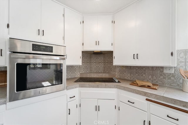 kitchen featuring stainless steel oven, backsplash, white cabinets, and black electric stovetop