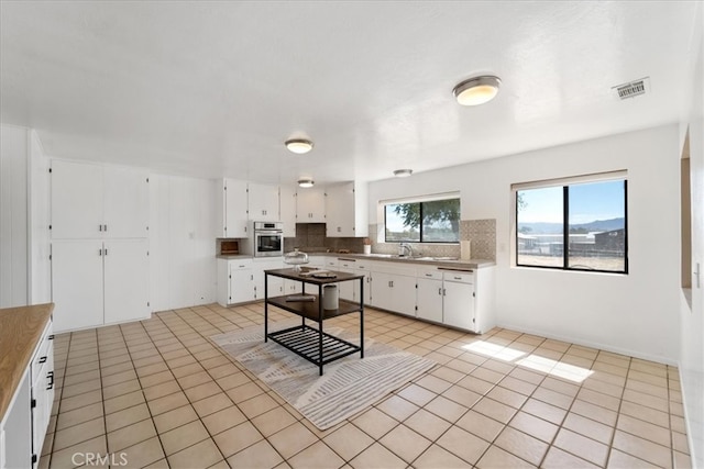 kitchen featuring decorative backsplash, sink, stainless steel oven, white cabinetry, and light tile patterned floors