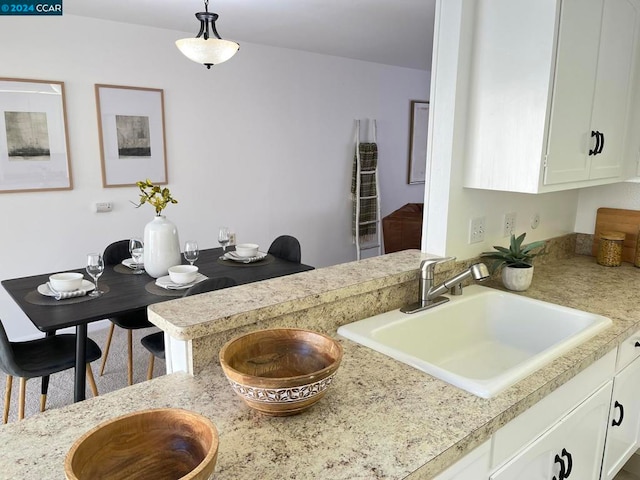 kitchen with kitchen peninsula, white cabinets, sink, and decorative light fixtures