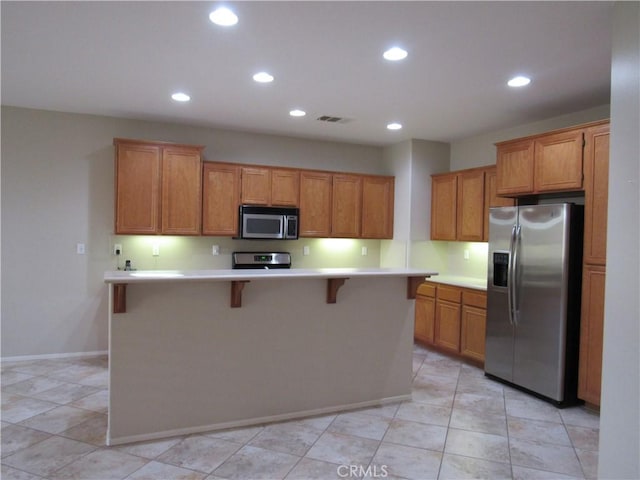 kitchen with a breakfast bar, light tile patterned floors, stainless steel appliances, and a kitchen island