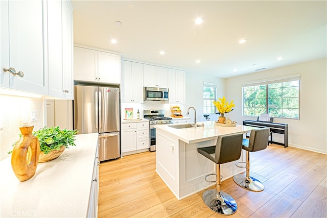 kitchen with sink, white cabinetry, light hardwood / wood-style flooring, appliances with stainless steel finishes, and a center island with sink