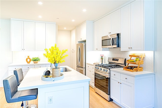 kitchen with stainless steel appliances, white cabinets, a breakfast bar area, light hardwood / wood-style flooring, and a center island with sink