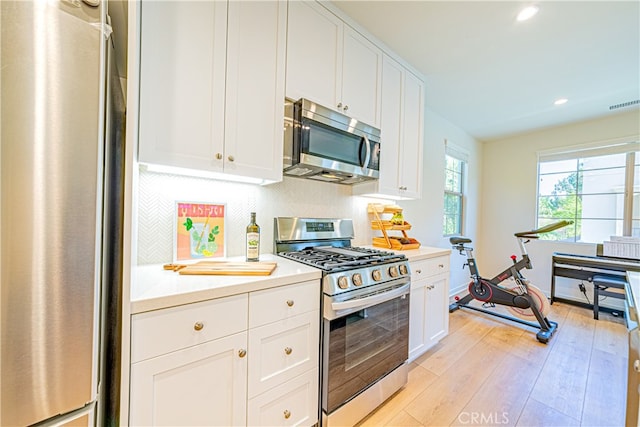 kitchen with appliances with stainless steel finishes, decorative backsplash, white cabinetry, and light hardwood / wood-style flooring