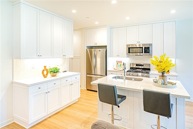 kitchen featuring a kitchen island with sink, sink, light hardwood / wood-style floors, white cabinetry, and appliances with stainless steel finishes