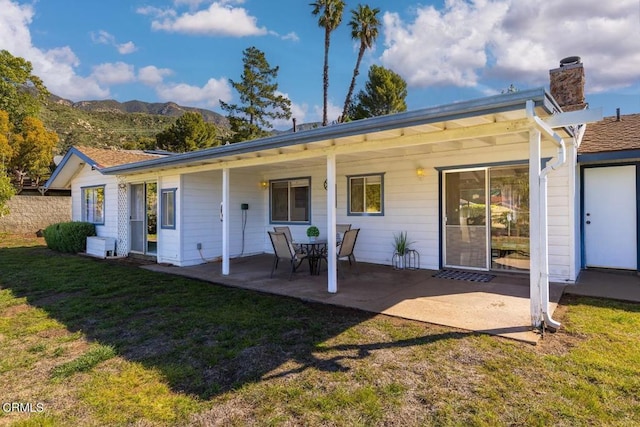 back of property with a mountain view, a patio area, and a yard