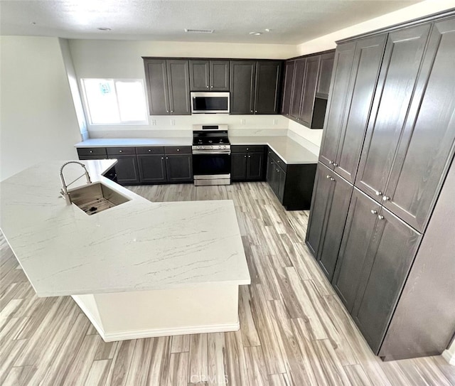 kitchen with a kitchen island with sink, stove, light hardwood / wood-style flooring, sink, and light stone countertops