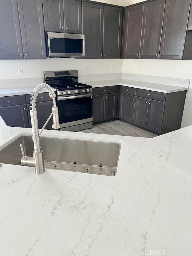 kitchen featuring light stone countertops, appliances with stainless steel finishes, sink, and dark brown cabinets