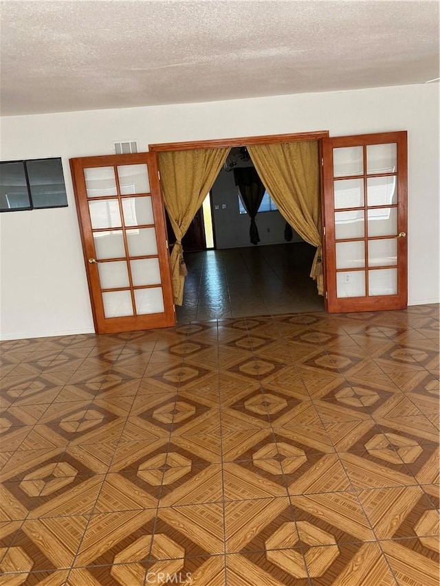 spare room with dark parquet flooring, french doors, and a textured ceiling