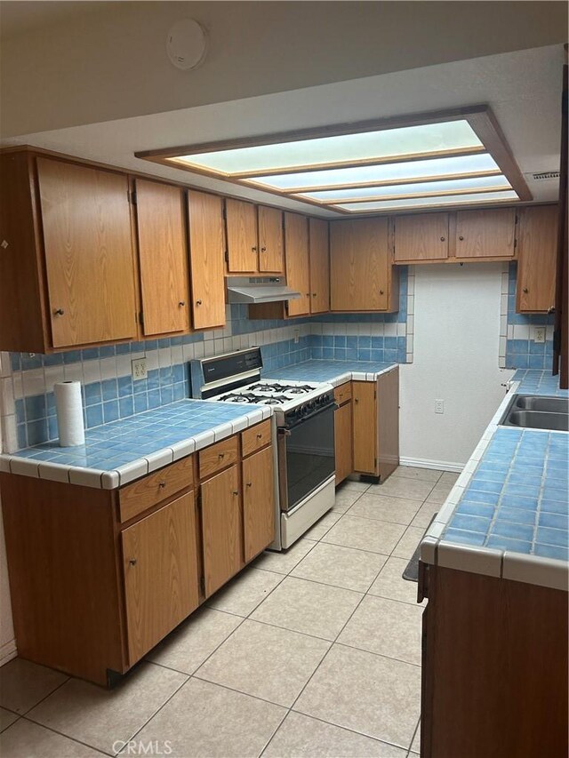 kitchen with tile countertops, white range, a skylight, decorative backsplash, and light tile patterned flooring