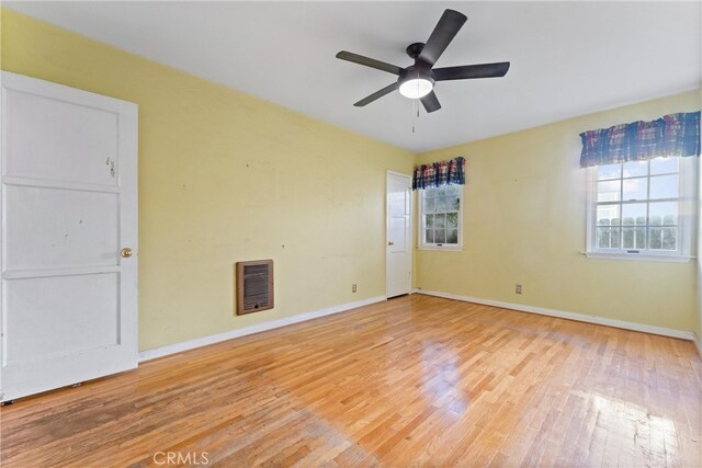 spare room with heating unit, ceiling fan, hardwood / wood-style floors, and a healthy amount of sunlight