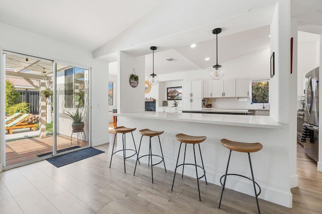 kitchen with pendant lighting, lofted ceiling, white cabinets, stainless steel fridge, and kitchen peninsula