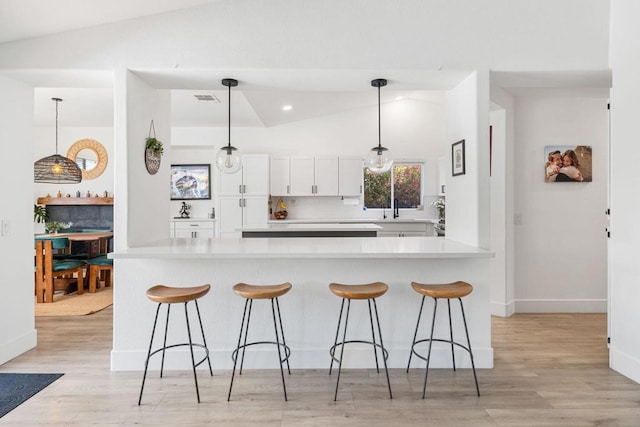 kitchen featuring light wood-type flooring, pendant lighting, vaulted ceiling, and white cabinetry