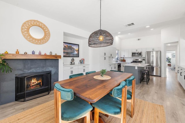 dining space with sink, light hardwood / wood-style floors, and a tiled fireplace