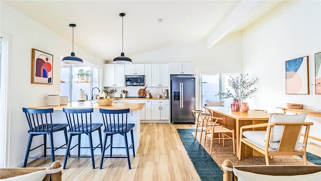 kitchen featuring pendant lighting, beamed ceiling, white cabinets, light hardwood / wood-style flooring, and stainless steel appliances