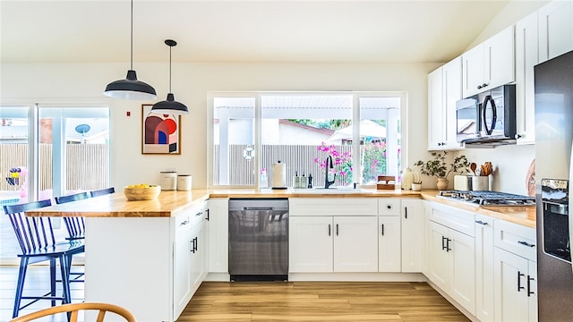 kitchen with pendant lighting, white cabinetry, stainless steel appliances, light wood-type flooring, and butcher block counters