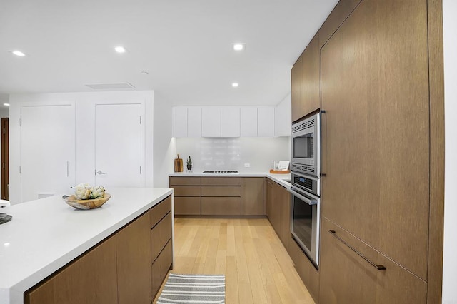 kitchen with stainless steel appliances, white cabinets, decorative backsplash, and light hardwood / wood-style flooring