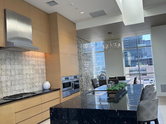 kitchen featuring stainless steel appliances, an island with sink, dark stone counters, a kitchen bar, and wall chimney range hood