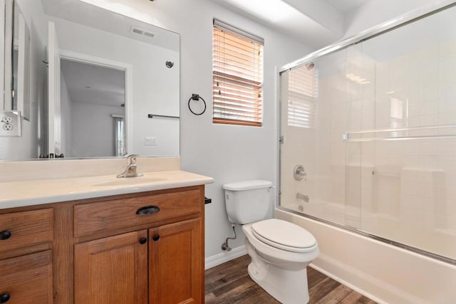 full bathroom with bath / shower combo with glass door, hardwood / wood-style flooring, vanity, and toilet