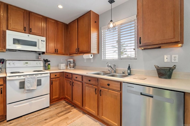 kitchen featuring light wood-type flooring, pendant lighting, white appliances, and sink