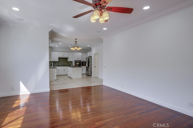 unfurnished living room with crown molding, ceiling fan with notable chandelier, and light hardwood / wood-style floors