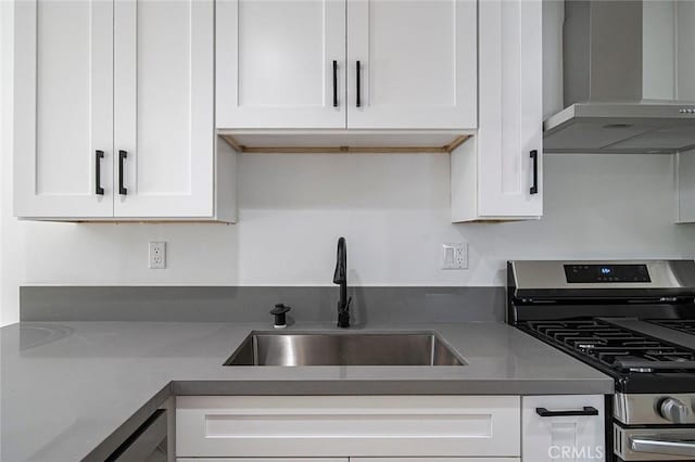 kitchen featuring dishwasher, white cabinets, stainless steel range with gas cooktop, sink, and wall chimney exhaust hood