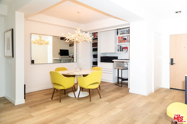 dining room featuring a tray ceiling, an inviting chandelier, and light hardwood / wood-style flooring