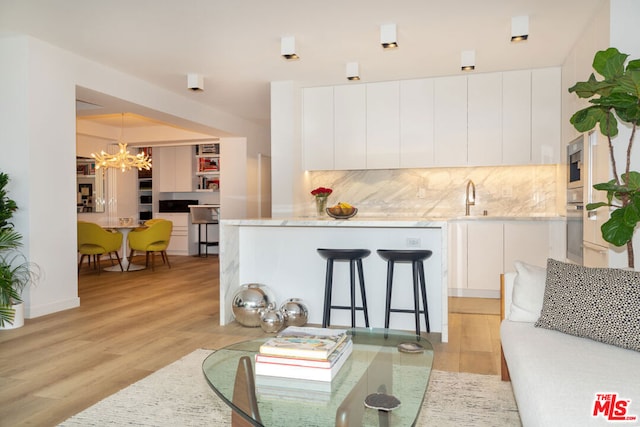 kitchen with light wood-type flooring, tasteful backsplash, white cabinets, appliances with stainless steel finishes, and decorative light fixtures