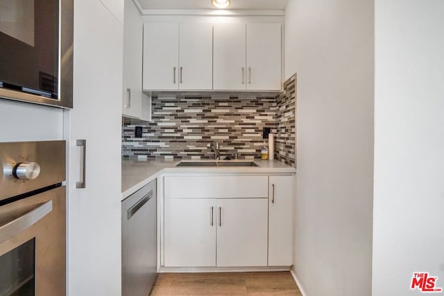 kitchen with backsplash, sink, light wood-type flooring, appliances with stainless steel finishes, and white cabinetry