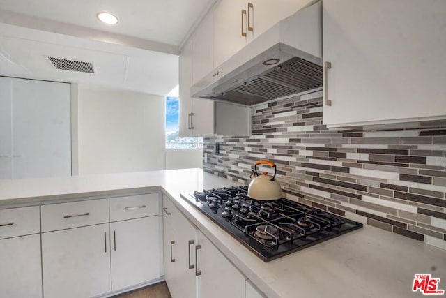 kitchen featuring black gas stovetop, white cabinetry, kitchen peninsula, and tasteful backsplash