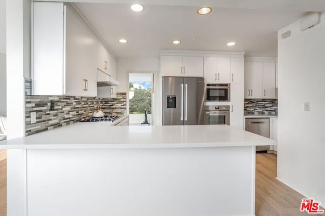 kitchen with kitchen peninsula, appliances with stainless steel finishes, light wood-type flooring, tasteful backsplash, and white cabinets